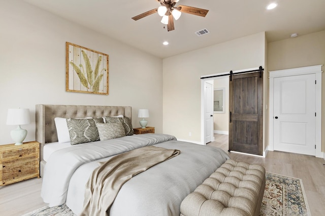 bedroom with ceiling fan, a barn door, and light hardwood / wood-style flooring