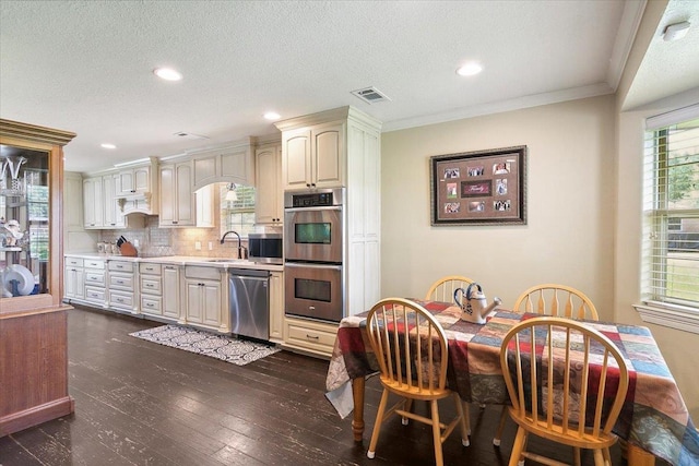 kitchen with dark wood-type flooring, crown molding, a textured ceiling, appliances with stainless steel finishes, and tasteful backsplash