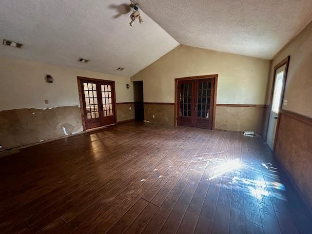 unfurnished living room featuring dark hardwood / wood-style floors, vaulted ceiling, french doors, and a textured ceiling
