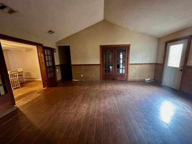 unfurnished living room featuring french doors, lofted ceiling, dark wood-type flooring, and a textured ceiling