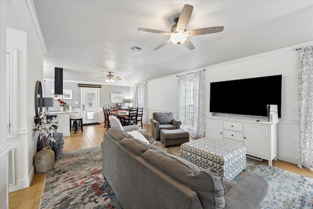 living room featuring visible vents, light wood finished floors, ceiling fan, ornamental molding, and wainscoting