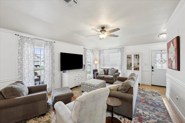 living area with visible vents, light wood-style flooring, ceiling fan, and ornamental molding