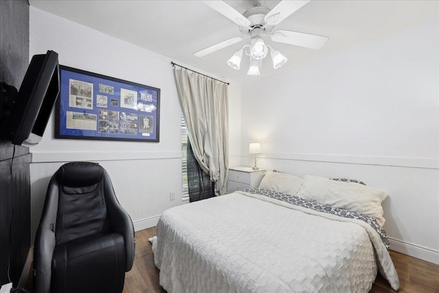 bedroom featuring a wainscoted wall, baseboards, wood finished floors, and a ceiling fan