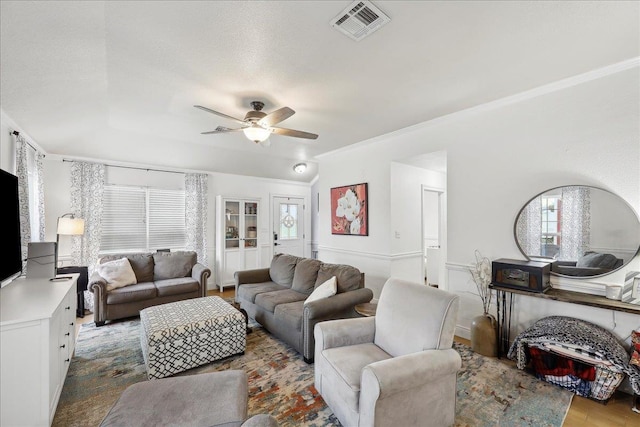 living room featuring wood finished floors, a ceiling fan, visible vents, and ornamental molding