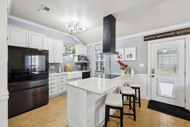 kitchen featuring a peninsula, refrigerator, stainless steel microwave, black electric stovetop, and island range hood