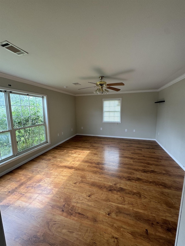 spare room with ceiling fan, baseboards, wood finished floors, visible vents, and ornamental molding