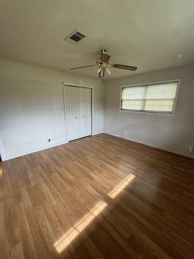 unfurnished bedroom with a ceiling fan, a textured ceiling, visible vents, and wood finished floors
