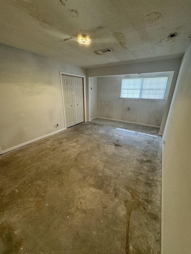 empty room featuring a textured ceiling, visible vents, baseboards, and unfinished concrete floors
