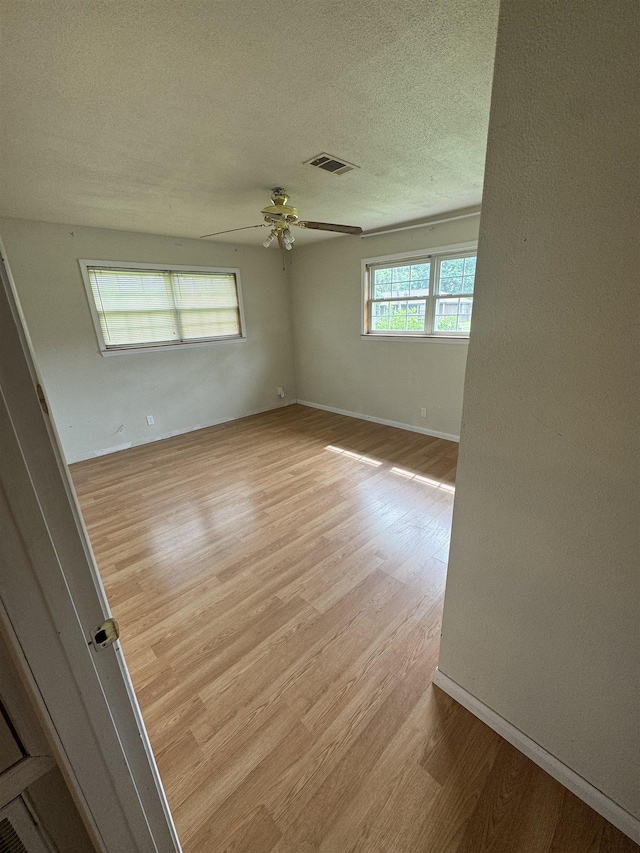 spare room featuring a textured ceiling, a ceiling fan, baseboards, light wood-type flooring, and visible vents
