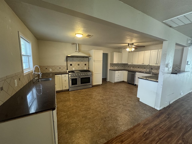 kitchen featuring wall chimney range hood, white cabinets, appliances with stainless steel finishes, a sink, and visible vents