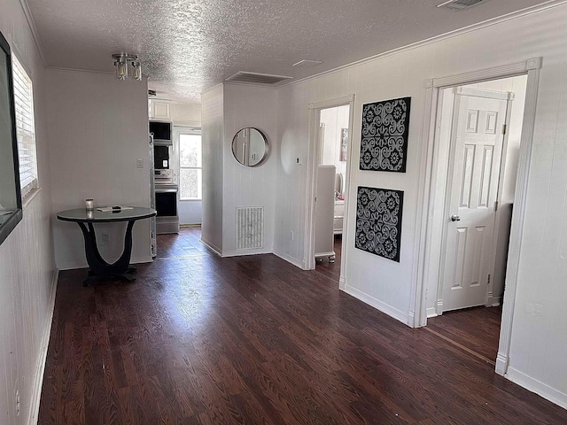 corridor with visible vents, a textured ceiling, dark wood-style floors, and ornamental molding