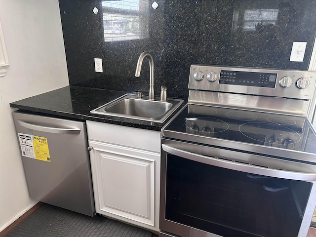 kitchen featuring dark countertops, decorative backsplash, white cabinets, stainless steel appliances, and a sink