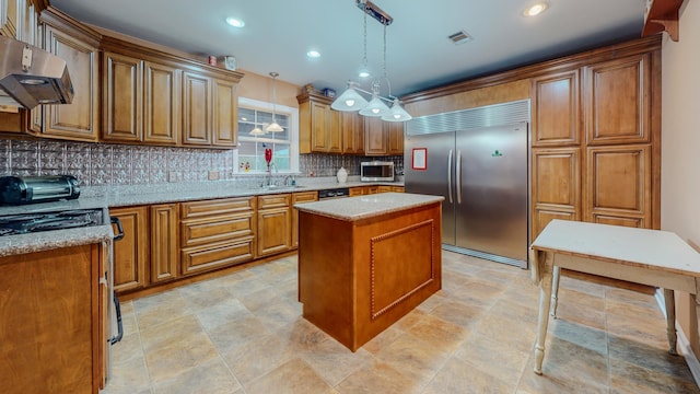 kitchen featuring a center island, appliances with stainless steel finishes, decorative light fixtures, light stone counters, and extractor fan