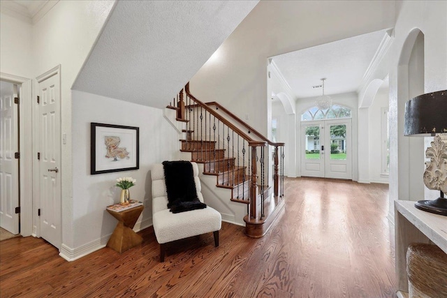 foyer featuring stairs, arched walkways, french doors, and wood finished floors
