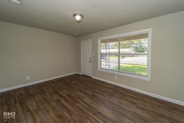 empty room featuring a textured ceiling, dark wood-type flooring, visible vents, and baseboards