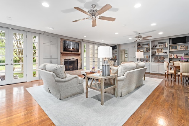 living room featuring ceiling fan, built in features, light hardwood / wood-style floors, and a brick fireplace