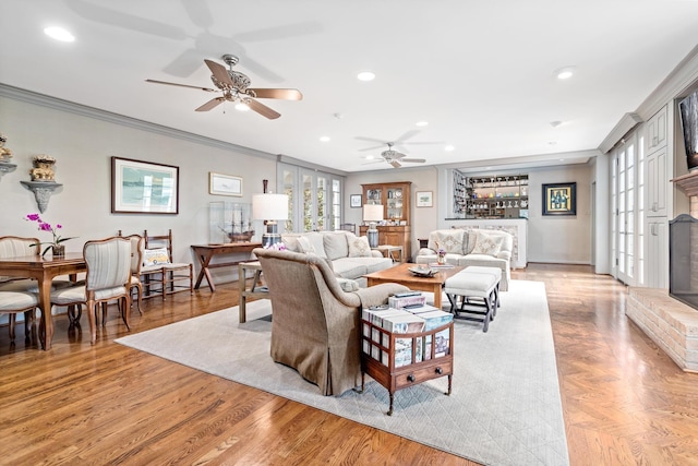 living room with a fireplace, light hardwood / wood-style floors, ceiling fan, and crown molding