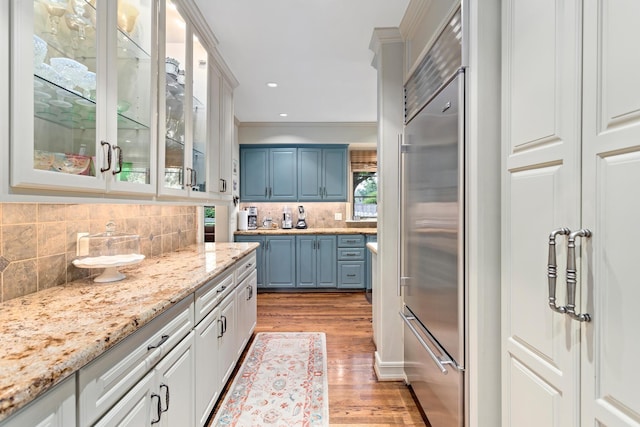 kitchen featuring white cabinets, blue cabinetry, built in fridge, and tasteful backsplash