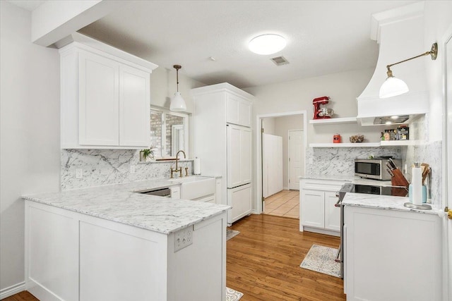 kitchen with decorative backsplash, kitchen peninsula, light stone counters, pendant lighting, and white cabinetry