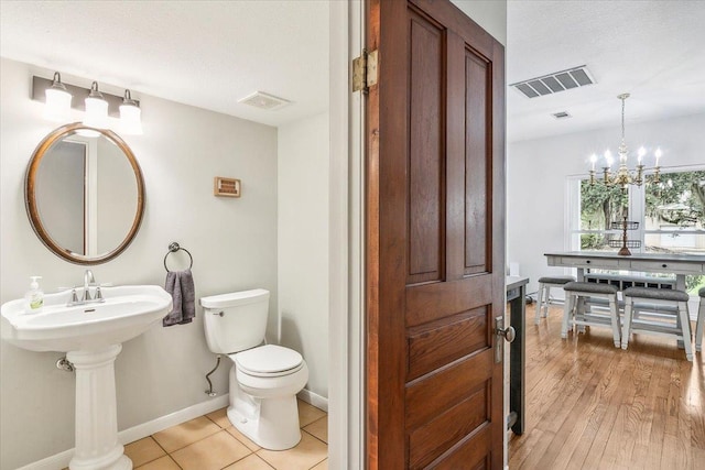 bathroom with hardwood / wood-style floors, a textured ceiling, toilet, and a notable chandelier