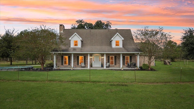 new england style home with covered porch and a yard