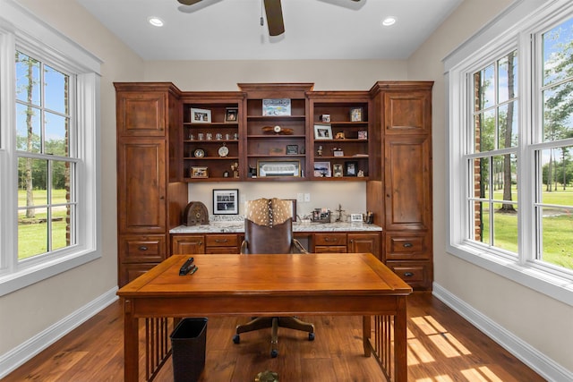 home office with a wealth of natural light, built in desk, and dark hardwood / wood-style floors