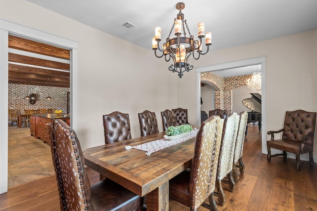 dining space with hardwood / wood-style floors, a notable chandelier, and brick wall