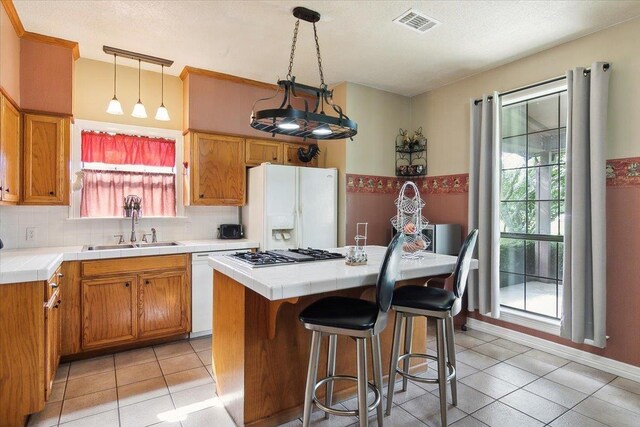 kitchen with tile countertops, white appliances, sink, hanging light fixtures, and a kitchen island