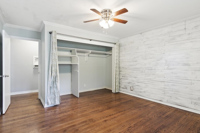 unfurnished bedroom featuring crown molding, dark wood-type flooring, ceiling fan, wooden walls, and a closet