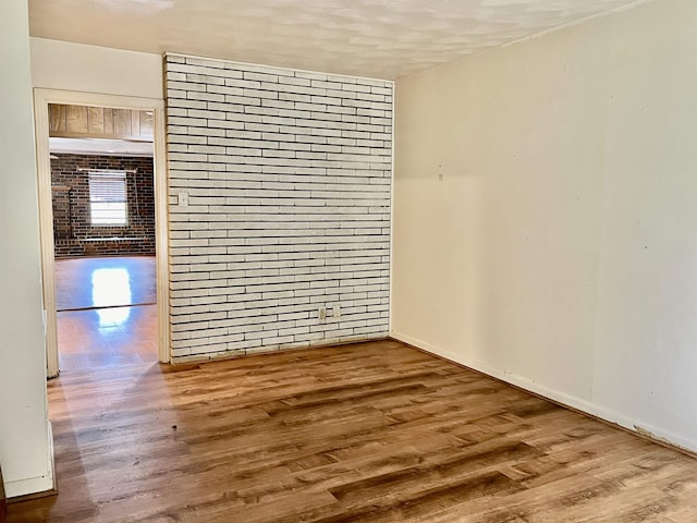 unfurnished room featuring hardwood / wood-style flooring and brick wall