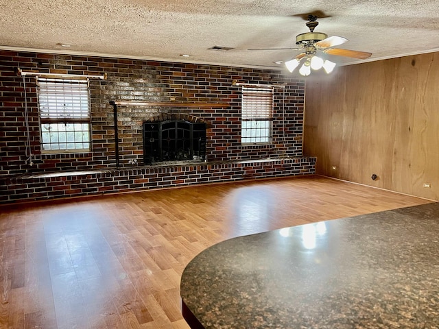 unfurnished living room featuring wood walls, hardwood / wood-style flooring, ceiling fan, a fireplace, and brick wall