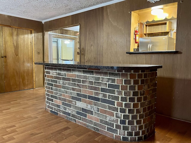 bar with stainless steel refrigerator, ornamental molding, wood walls, a textured ceiling, and hardwood / wood-style flooring