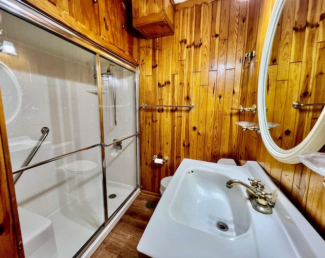 bathroom with sink, walk in shower, wood-type flooring, toilet, and wooden walls