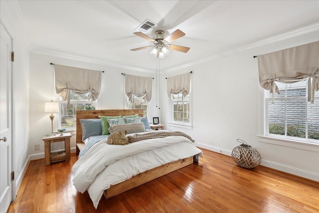 bedroom featuring hardwood / wood-style floors, visible vents, multiple windows, and ornamental molding