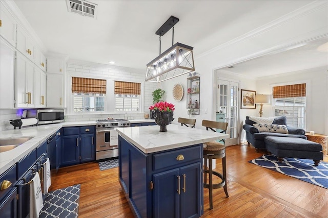 kitchen with visible vents, blue cabinetry, crown molding, a breakfast bar area, and appliances with stainless steel finishes