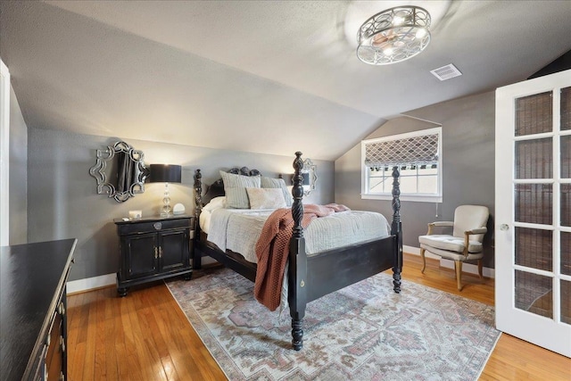 bedroom featuring visible vents, lofted ceiling, baseboards, and hardwood / wood-style floors