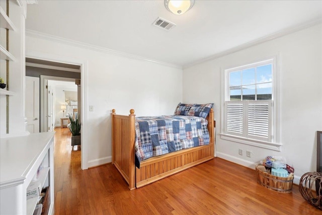 bedroom featuring visible vents, light wood-type flooring, baseboards, and ornamental molding