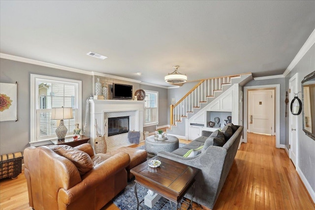 living area featuring stairway, visible vents, light wood-style flooring, a fireplace with flush hearth, and crown molding