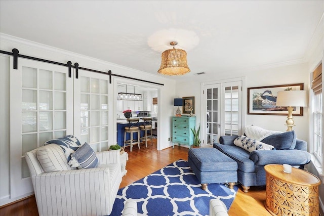 living room featuring wood finished floors, visible vents, ornamental molding, french doors, and a barn door