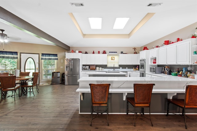 kitchen featuring white cabinetry, dark hardwood / wood-style floors, a tray ceiling, a kitchen bar, and appliances with stainless steel finishes