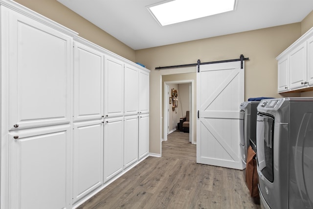 washroom with cabinets, a barn door, light hardwood / wood-style flooring, and washing machine and clothes dryer