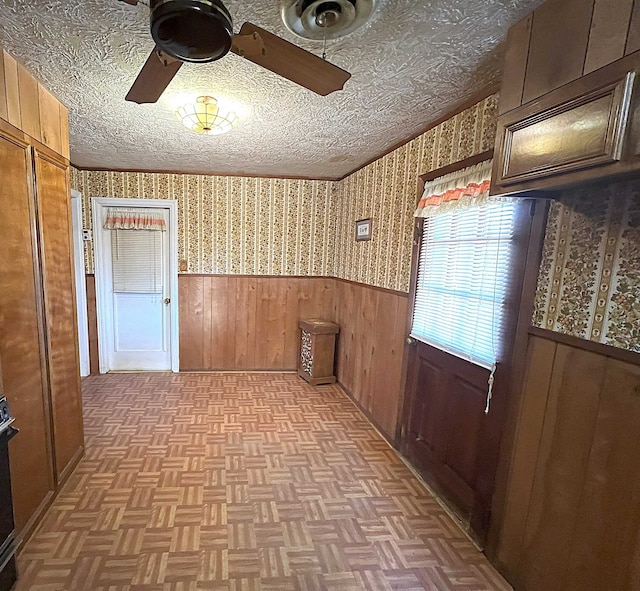 interior space featuring ceiling fan, wood walls, a textured ceiling, and light parquet floors