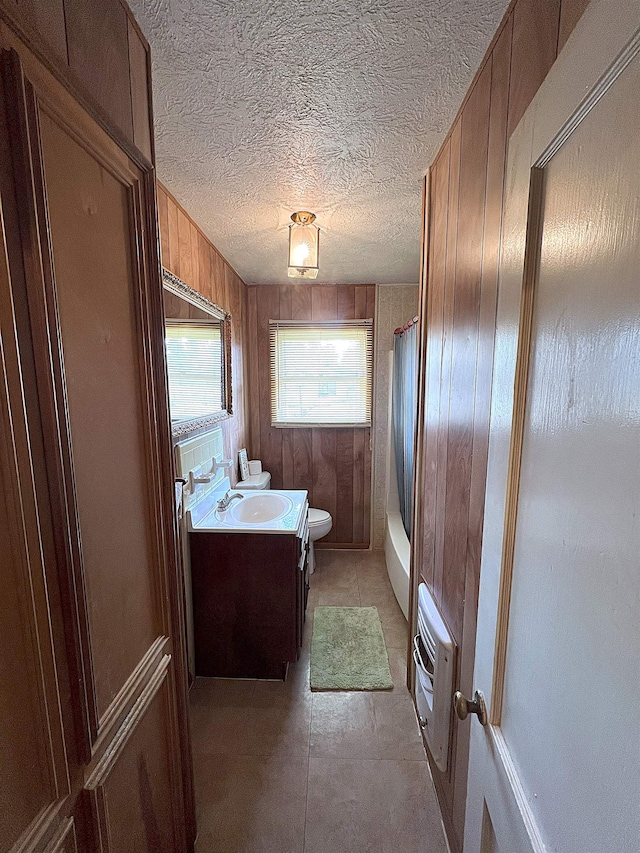 full bathroom featuring shower / tub combo with curtain, toilet, heating unit, vanity, and wooden walls