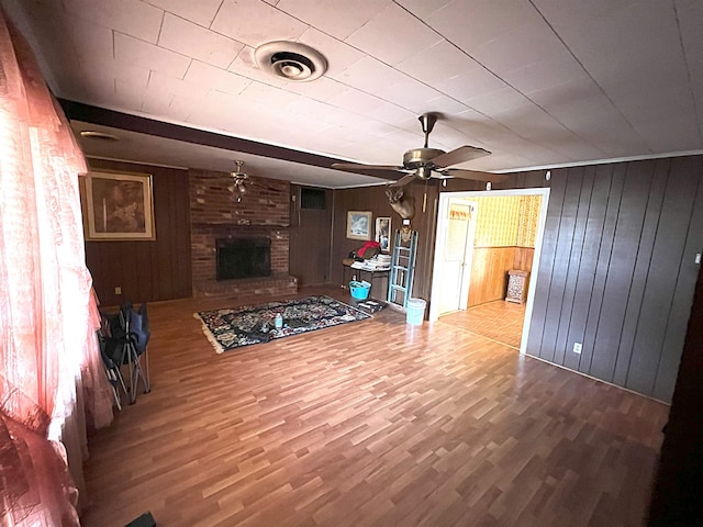 living room featuring wood-type flooring, a brick fireplace, ceiling fan, and wood walls