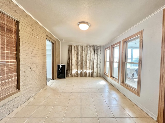 spare room with ornamental molding, light tile patterned flooring, a textured ceiling, and brick wall