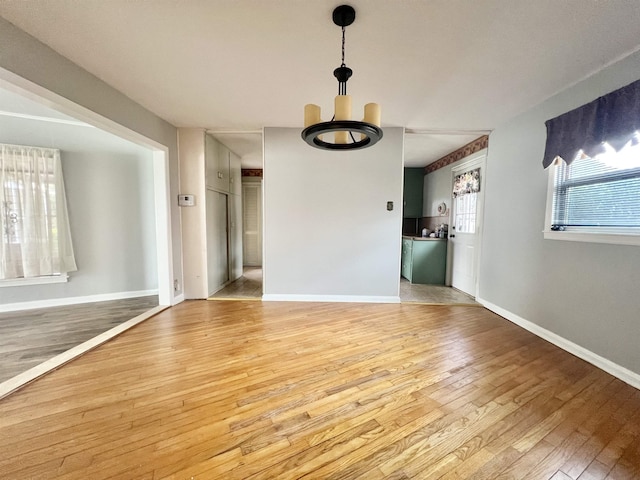 unfurnished room with light wood-style flooring, baseboards, and a chandelier