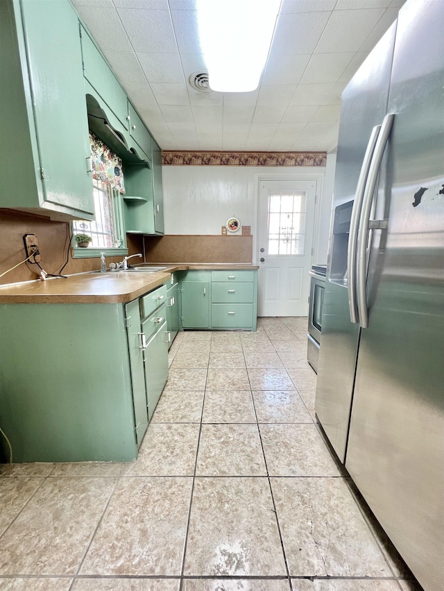 kitchen with light tile patterned floors, stainless steel fridge, visible vents, green cabinets, and a sink