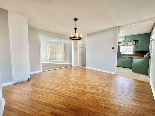 unfurnished dining area with light wood-type flooring, baseboards, and a notable chandelier