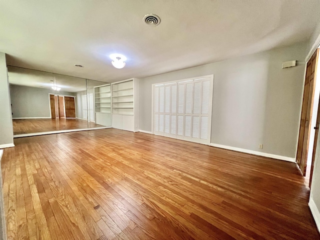 empty room with wood-type flooring, visible vents, baseboards, and built in features