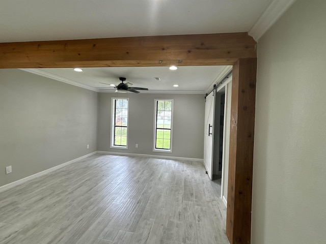 spare room with ceiling fan, ornamental molding, a barn door, and light hardwood / wood-style flooring